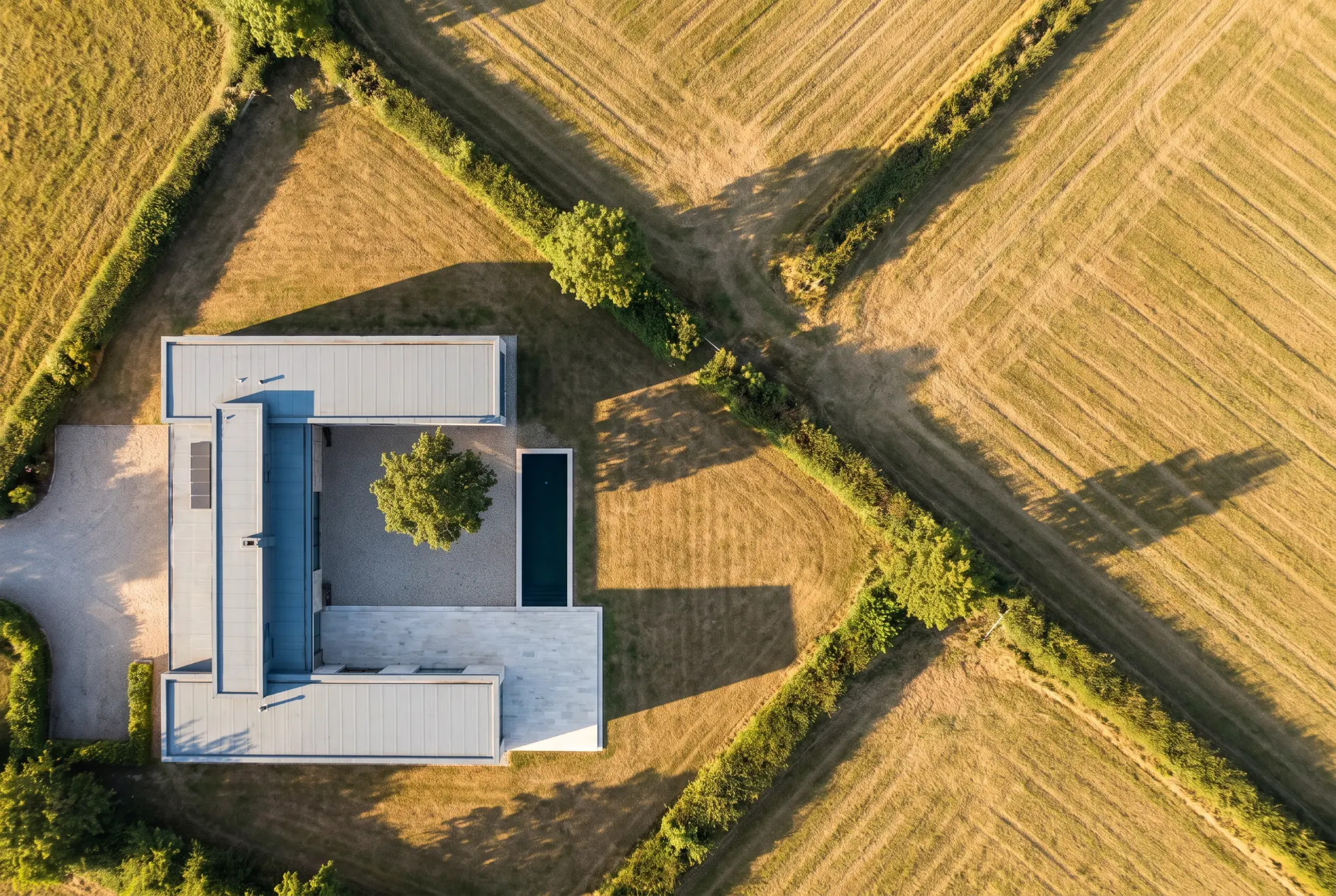Aerial view of the Longhouse: the roof reading as a single line drawn across hedgerow fields.