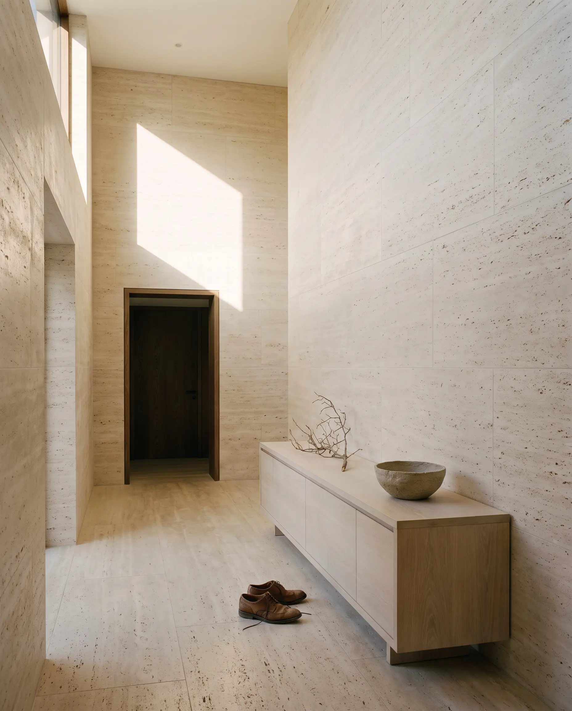 Entrance hall at Alder House: a stone floor, a single bench, and daylight from a high slot.