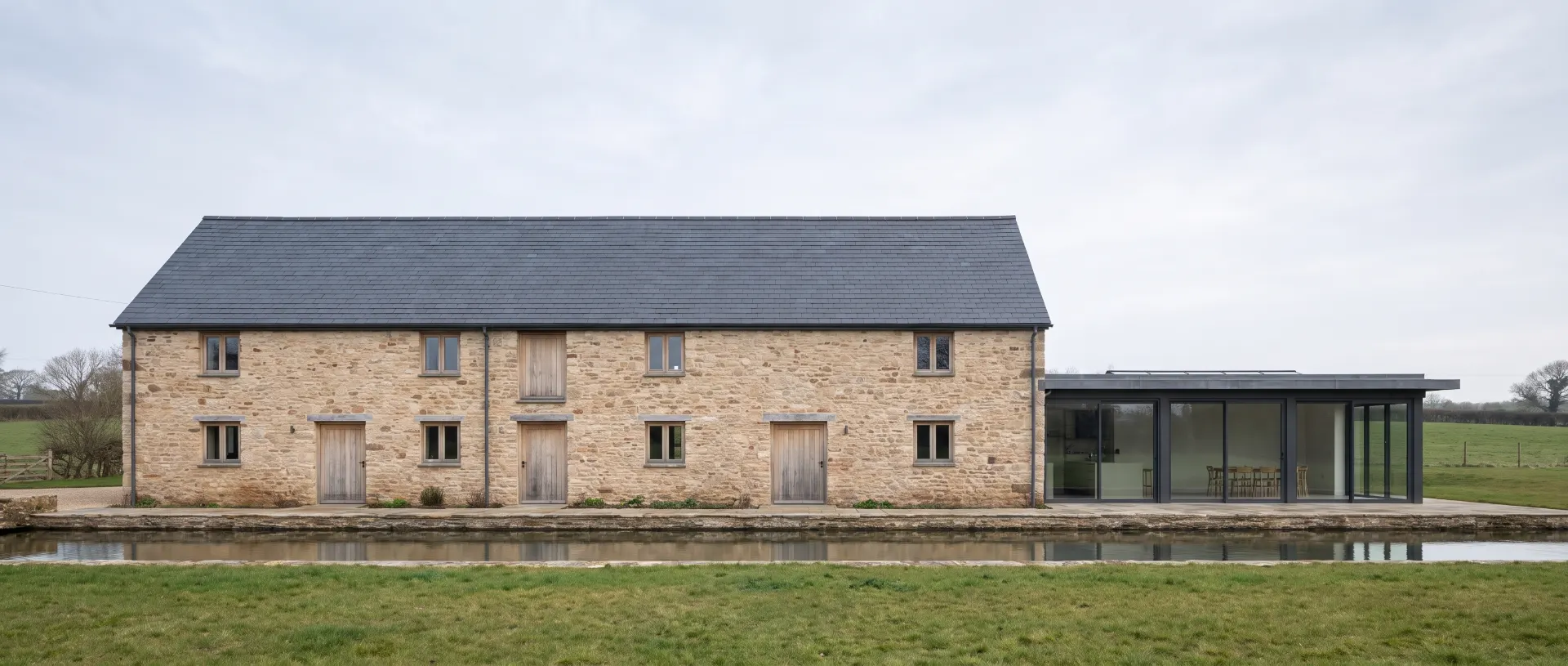 Mill House across the meadow, with a two-storey sandstone mill, slate roof, glazed extension and the mill leat running along the front.